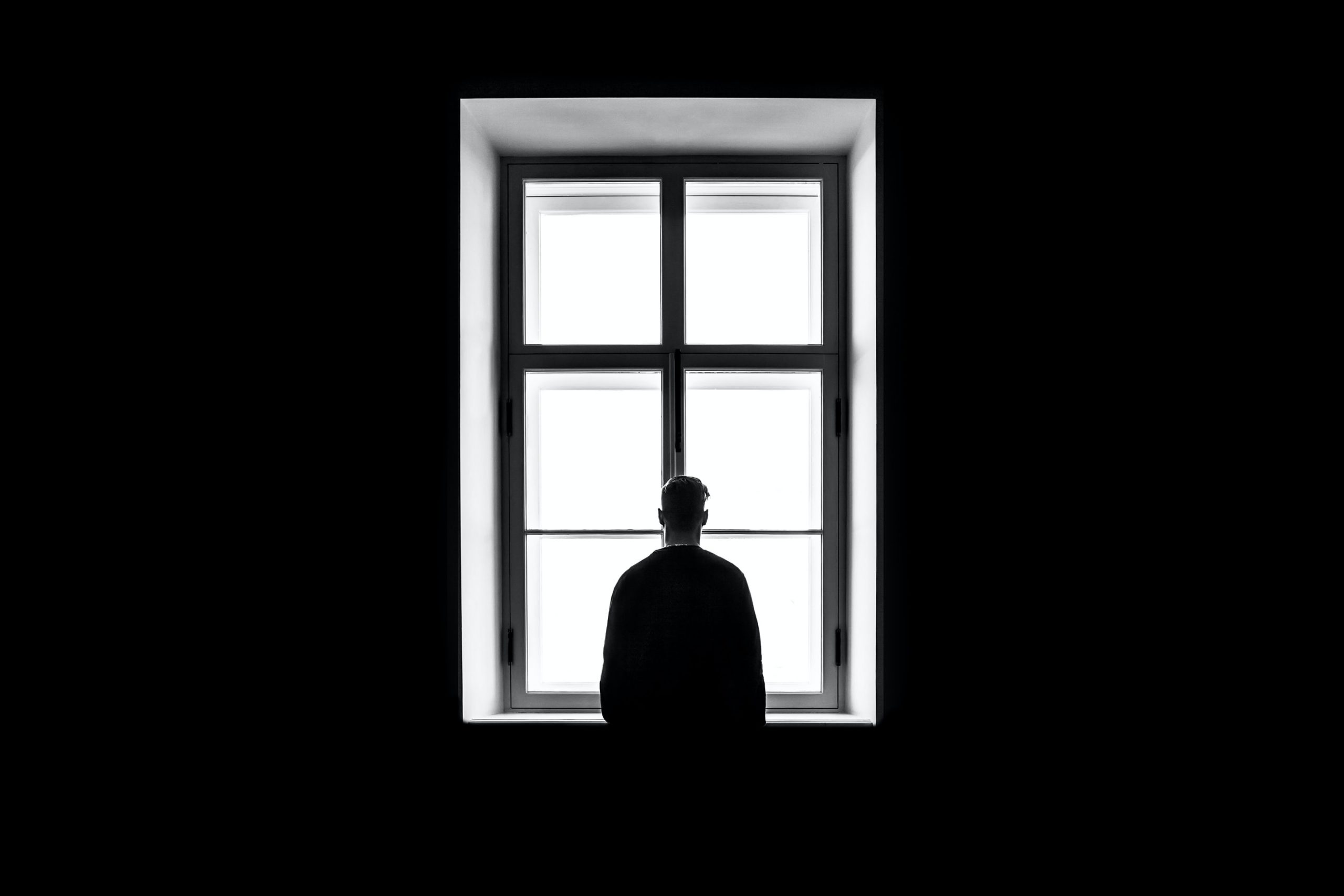 black and white image of man standing in front of window