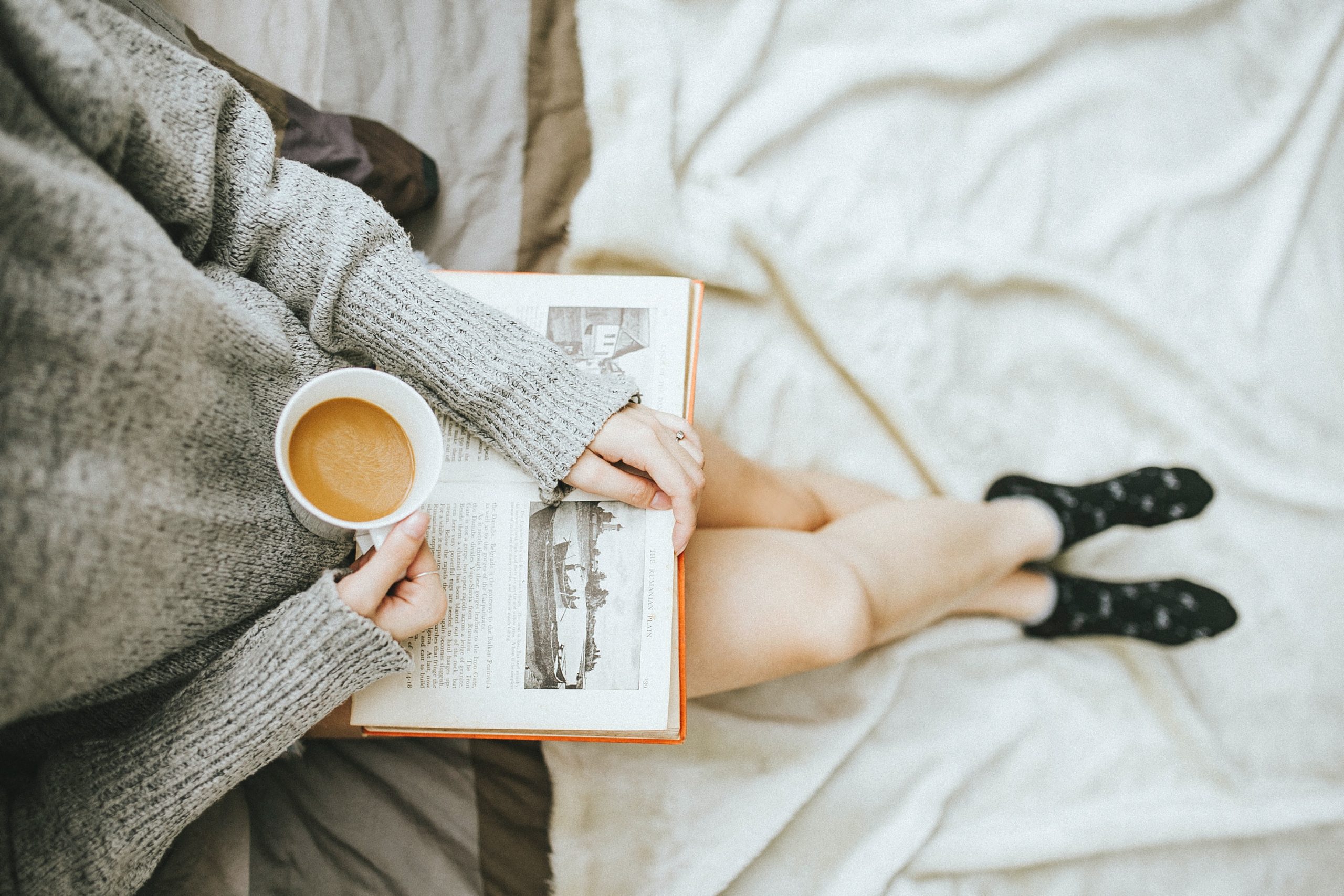 overhead shot of woman wearing grey jumper holding book and cup of tea