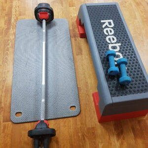 reebok step with blue dumbells next to black exercise mat with weighted barbell laid on top
