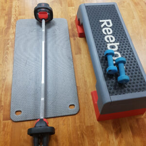 reebok step with blue dumbells next to black exercise mat with weighted barbell laid on top