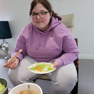 female in purple jumper holding plate of salad