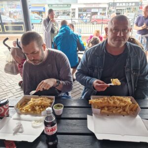 two male residents eating fish and chips on picnic bench