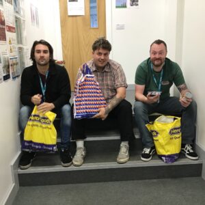 3 team members sitting on stairs holding bags of food