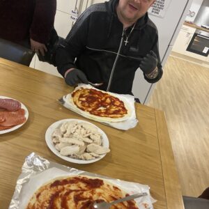 man adding pizza sauce to base