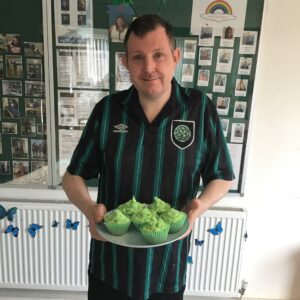 resident holding tray of cupcakes decorated with green icing