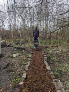 resident holding wheelbarrow on wood chip path