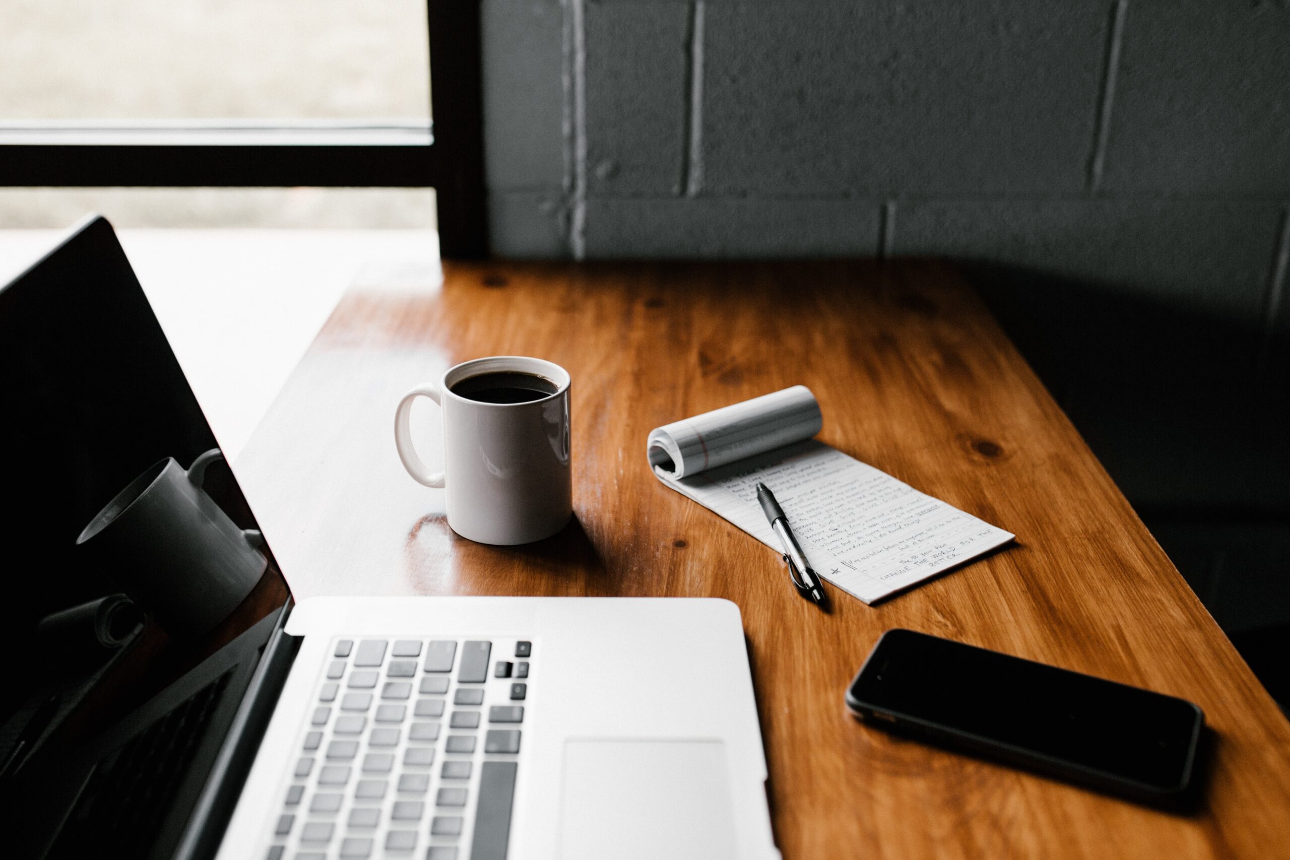 wooden desk with laptop, notepad and coffee cup on top