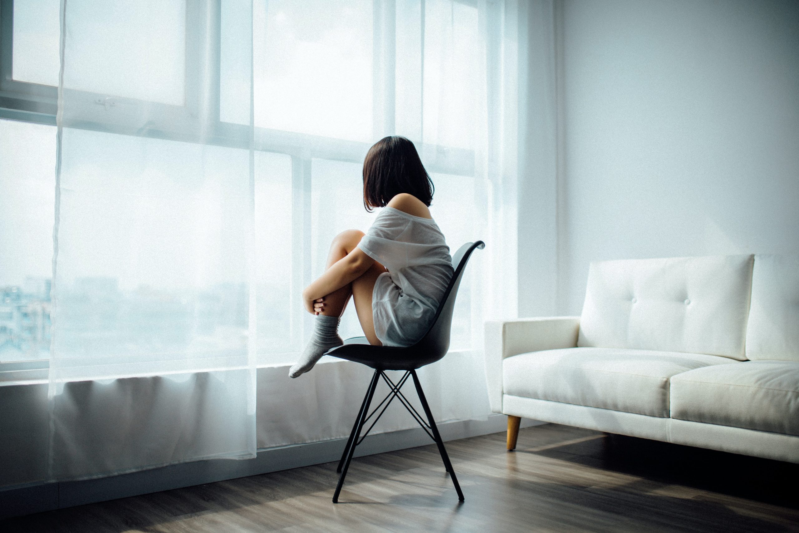 woman sitting on chair hugging knees looking out of window