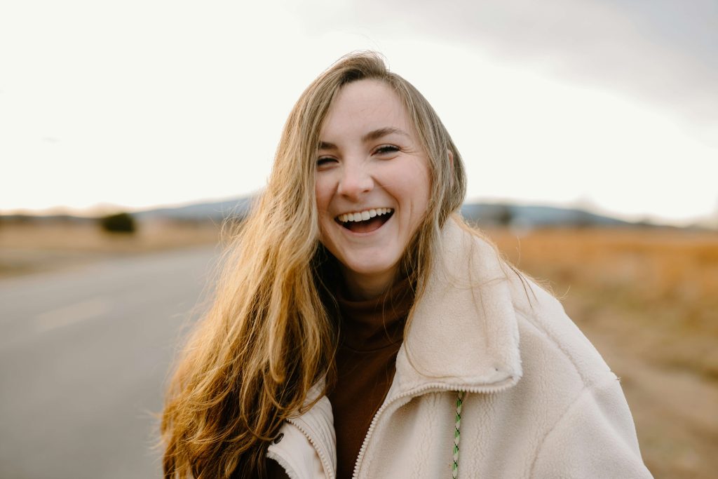 Woman outside wearing coat smiling and laughing for a blog about the mental health benefits of humour.