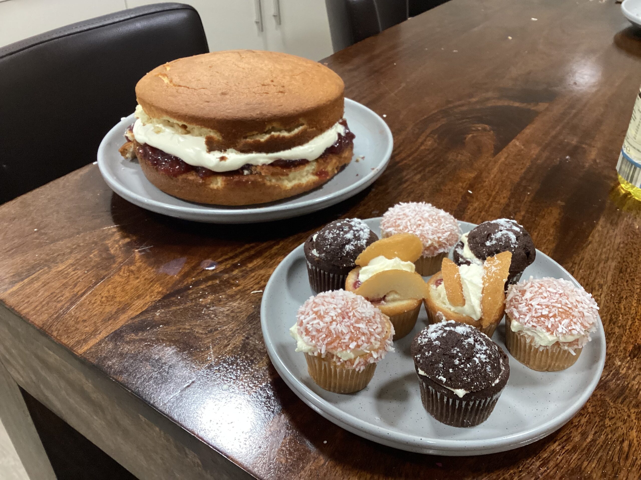 plate of cupcakes next to homemade victoria sponge cake