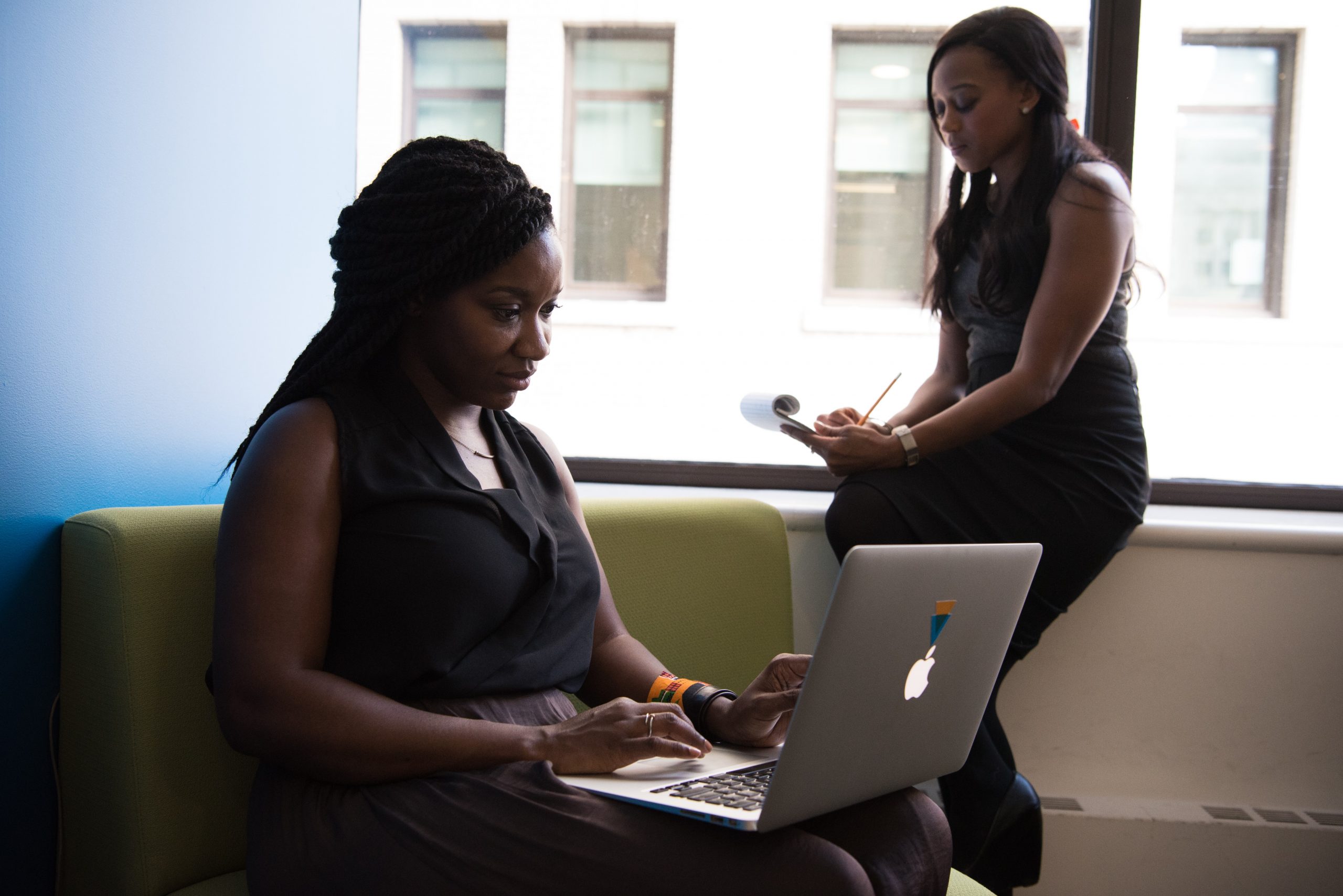 woman working on laptop and woman writing in notepad