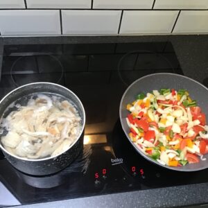 2 pans on hob, left with fish, right with veg