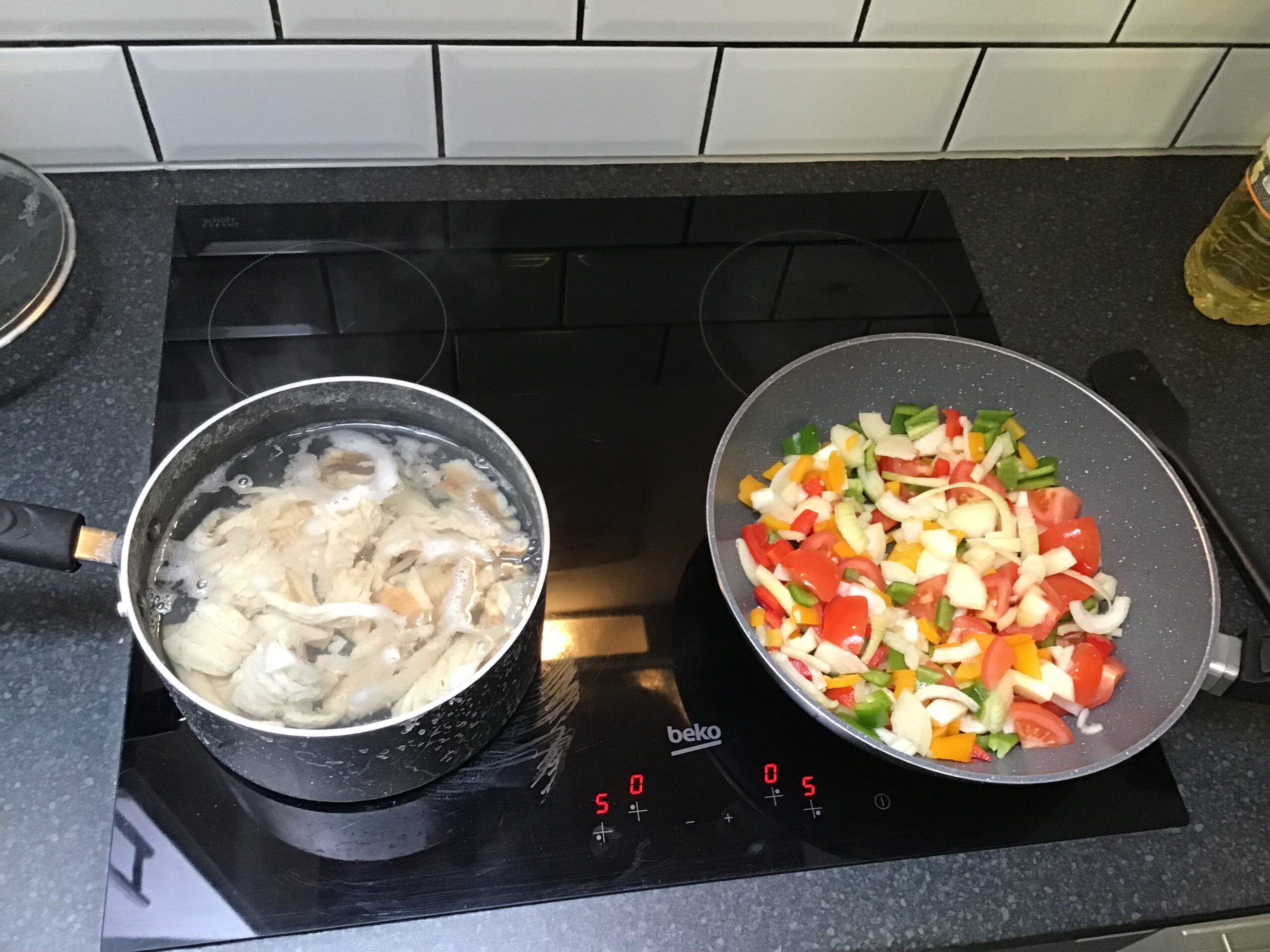2 pans on hob, left with fish, right with veg