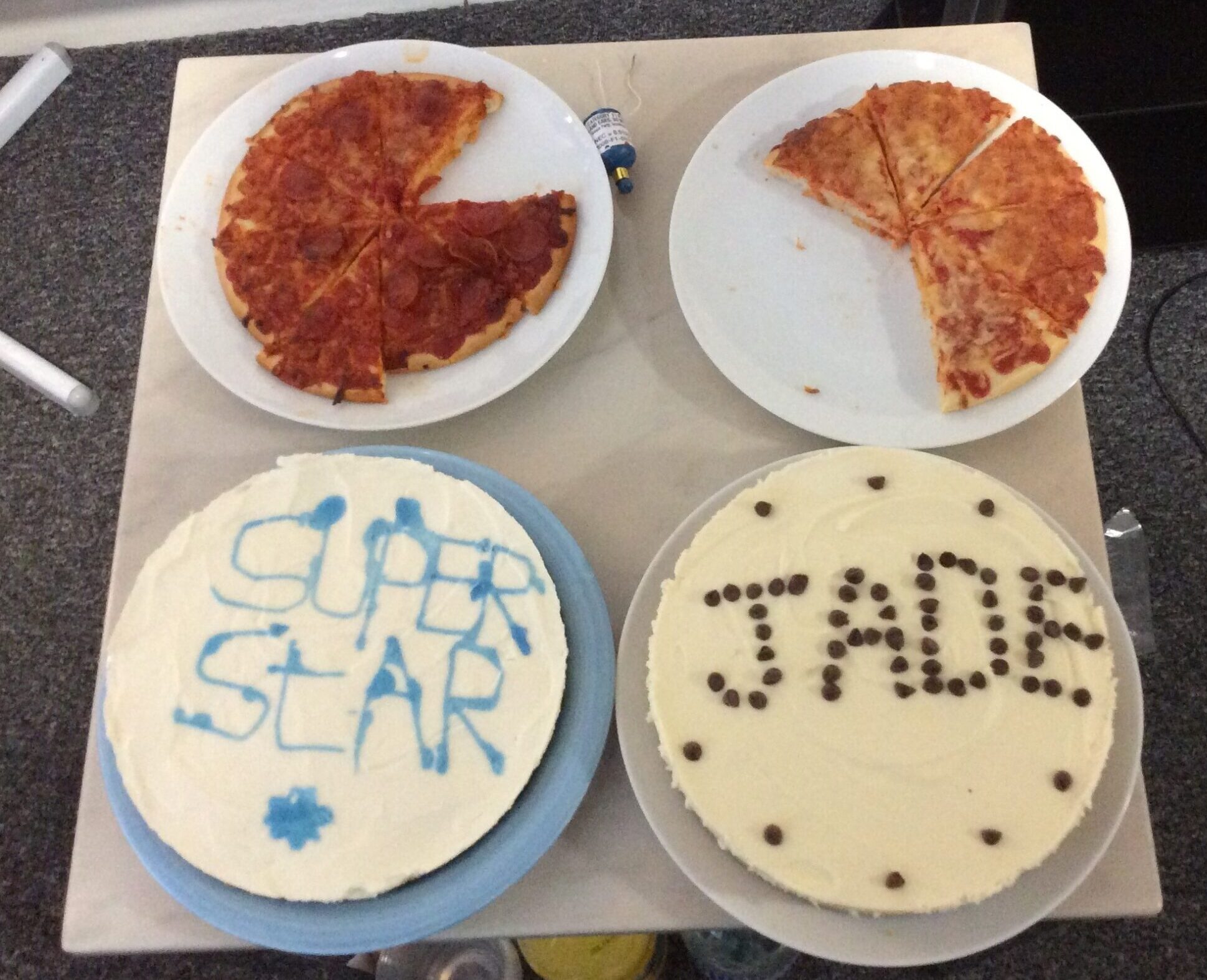 2 plates of pizza and two cakes, one iced "superstar" and one iced with "Jade"