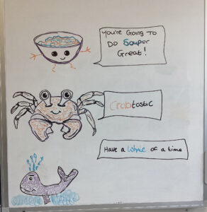 whiteboard with drawings of bowl of soup, crab and whale, and positive quote written next to the drawings