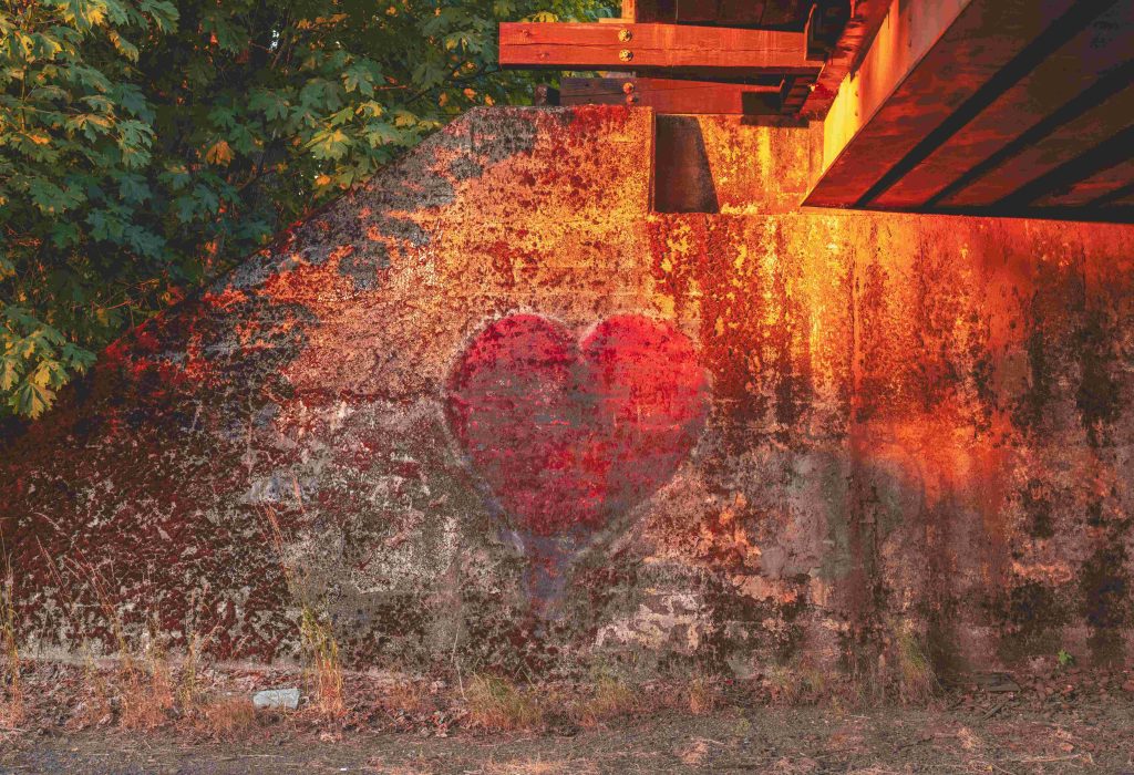 A red heart painted on an exterior wall with signs of dilapidation, for a blog about self-compassion and mental health.