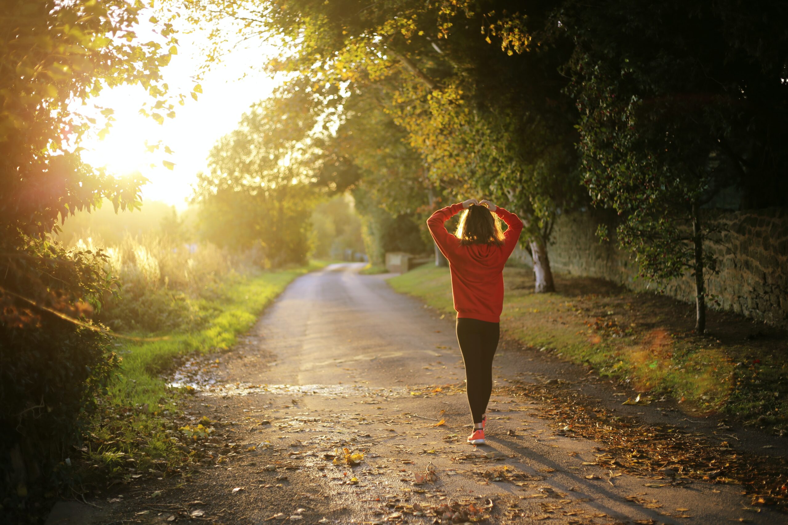 person in orange jacket walking along gravel path into sunlight
