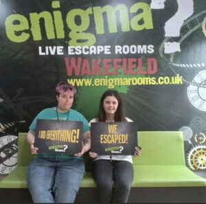 2 females outside escape room holding signs saying "we escaped" 