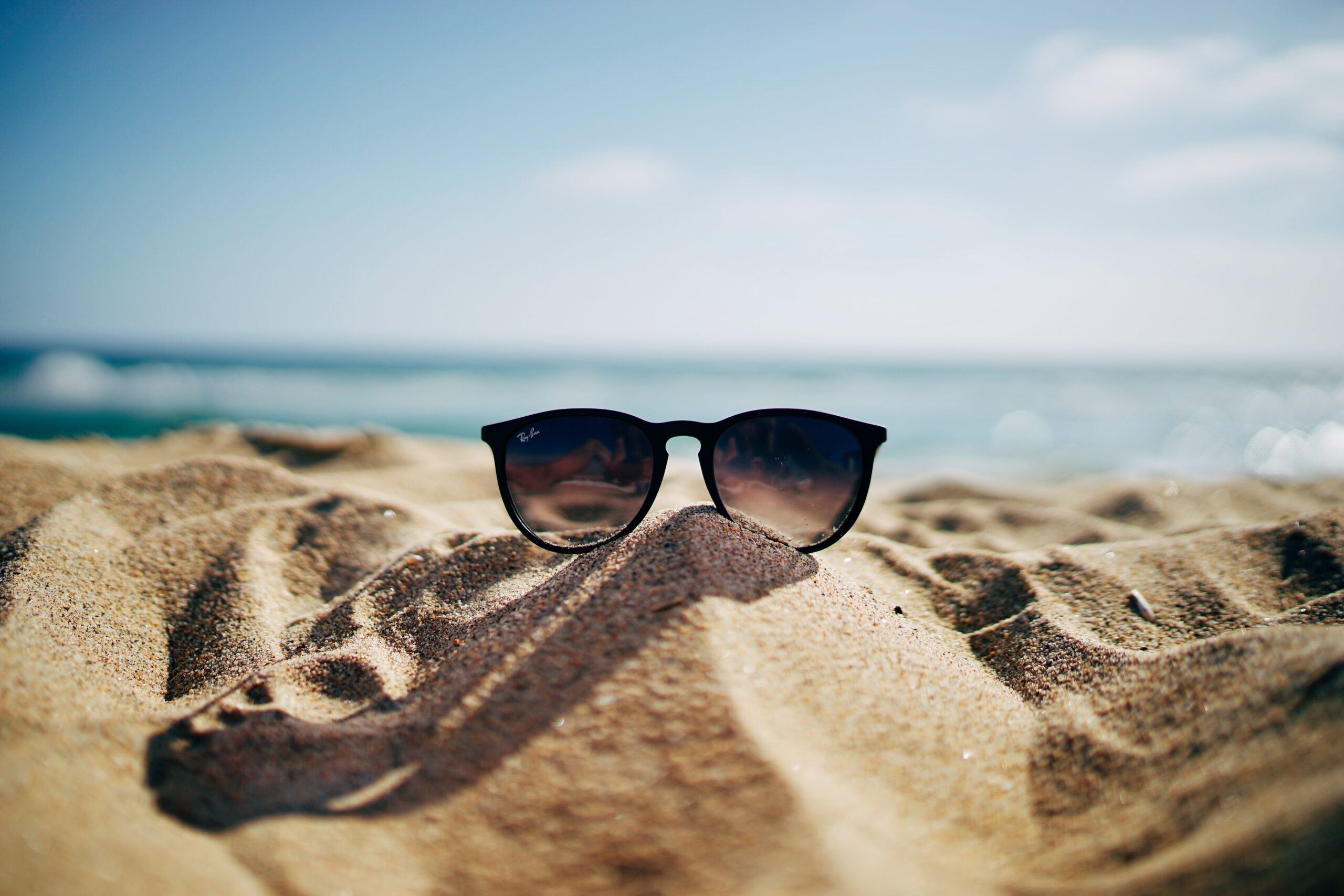 sunglasses on mound of sand with blue sky background