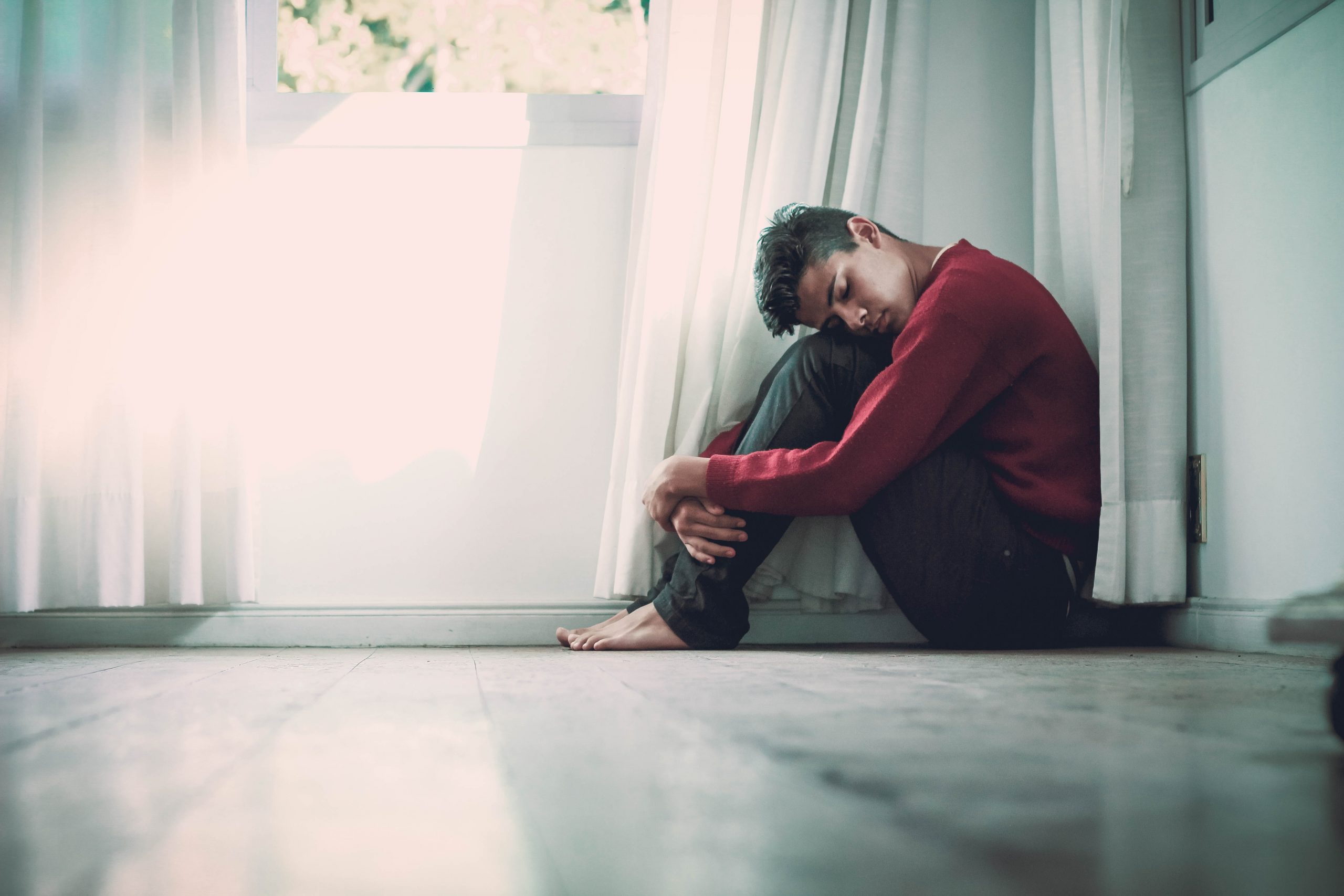 man sitting on floor with legs tucked up and head resting on knees