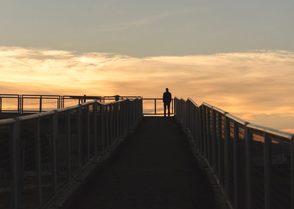 loneliness awareness week - silhouette of man on bridge against orange sunset