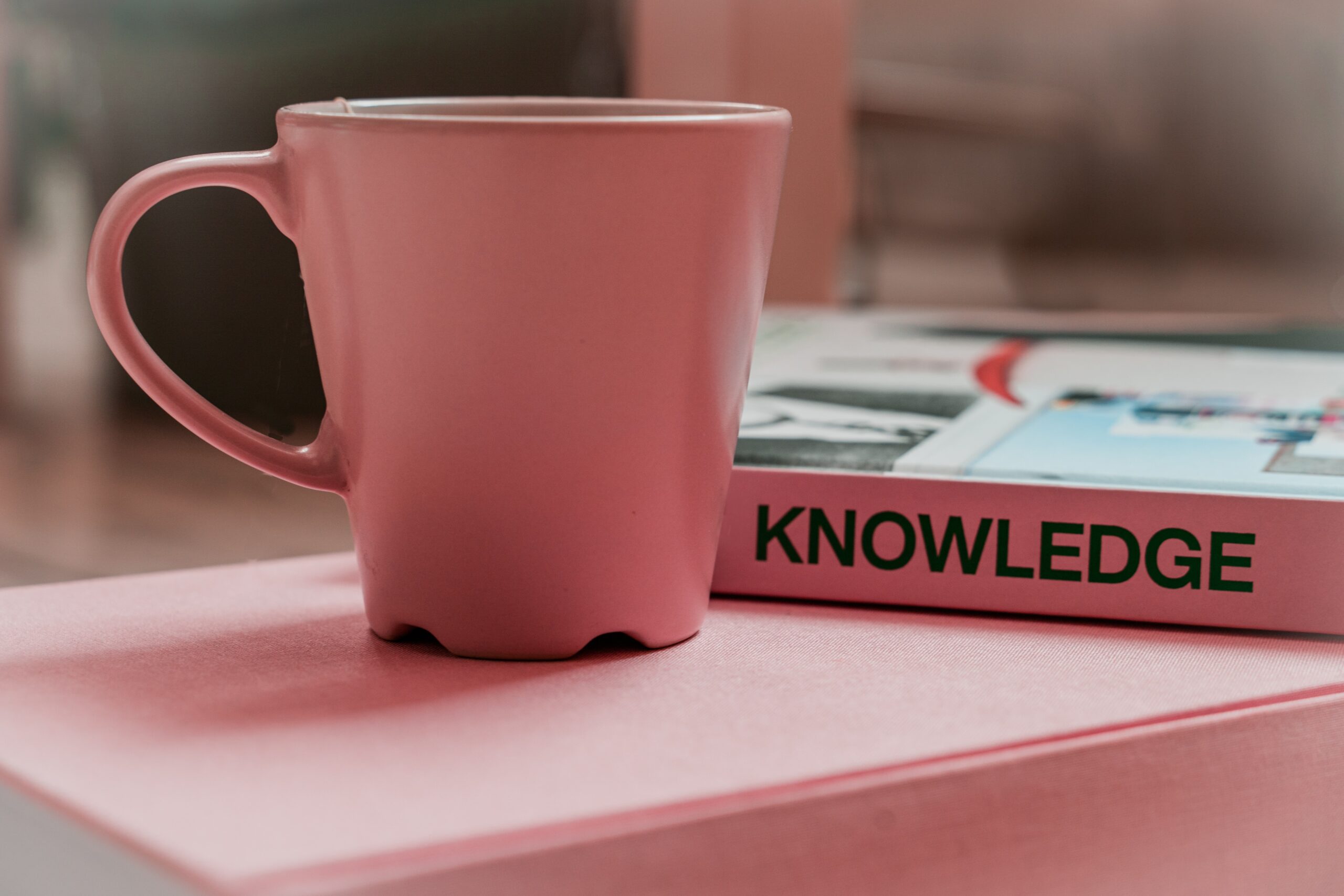pink mug next to pink book with knowledge written on spine