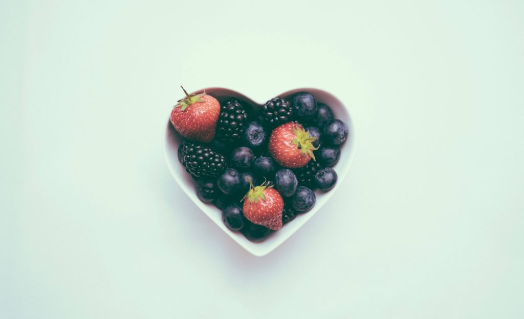 A heart-shaped bowl of berries on a plain background to represent gut health and its ties to mental health