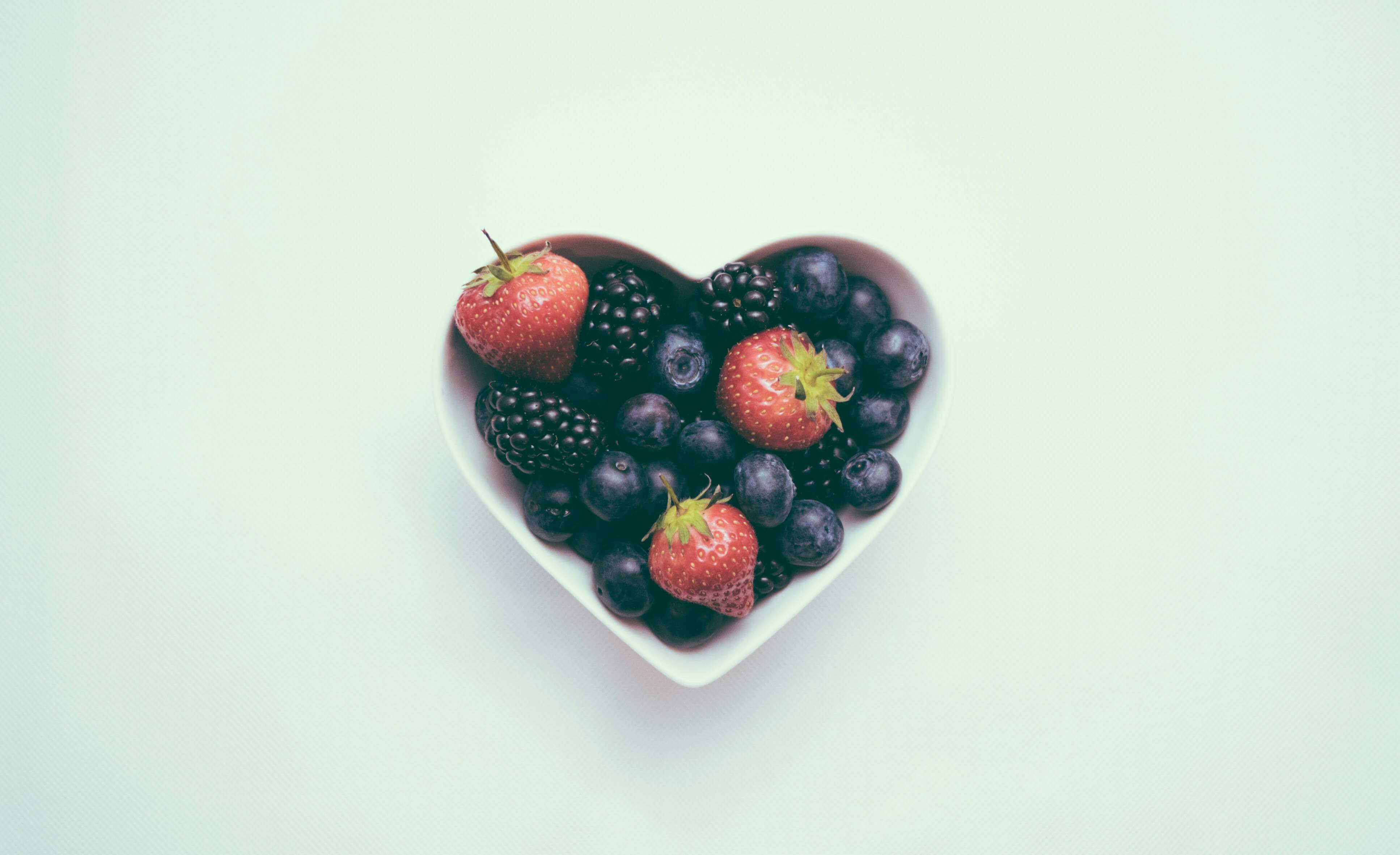 A heart-shaped bowl of berries on a plain background to represent gut health and its ties to mental health