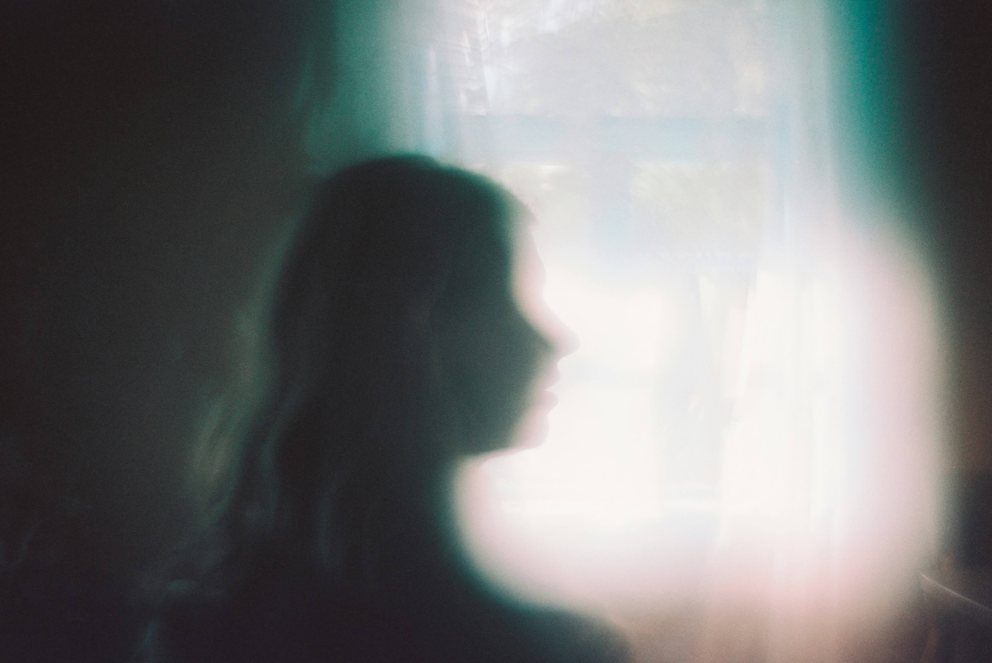 Person in hazed dark room with light coming through a window. A profile silhouette representing the feelings of PTSD.