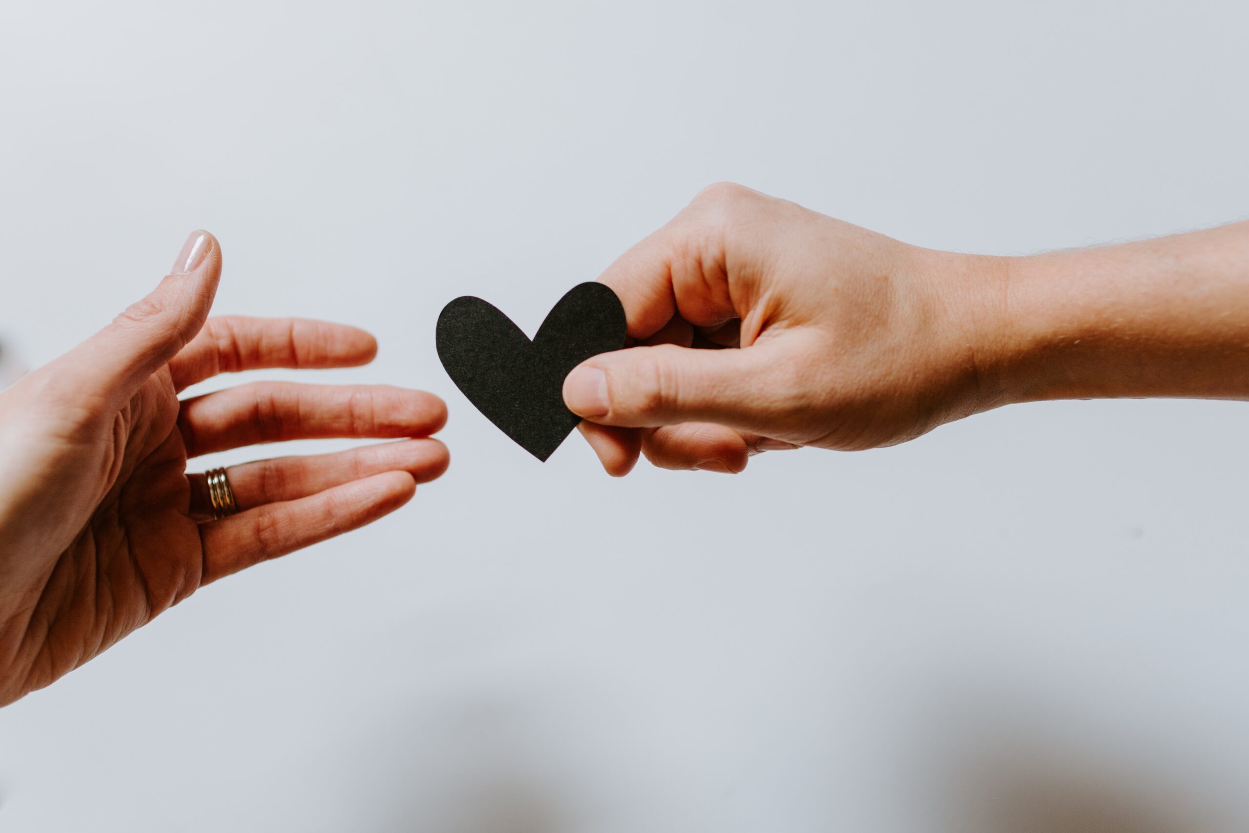 shot of hands one passing small, black paper heart to other