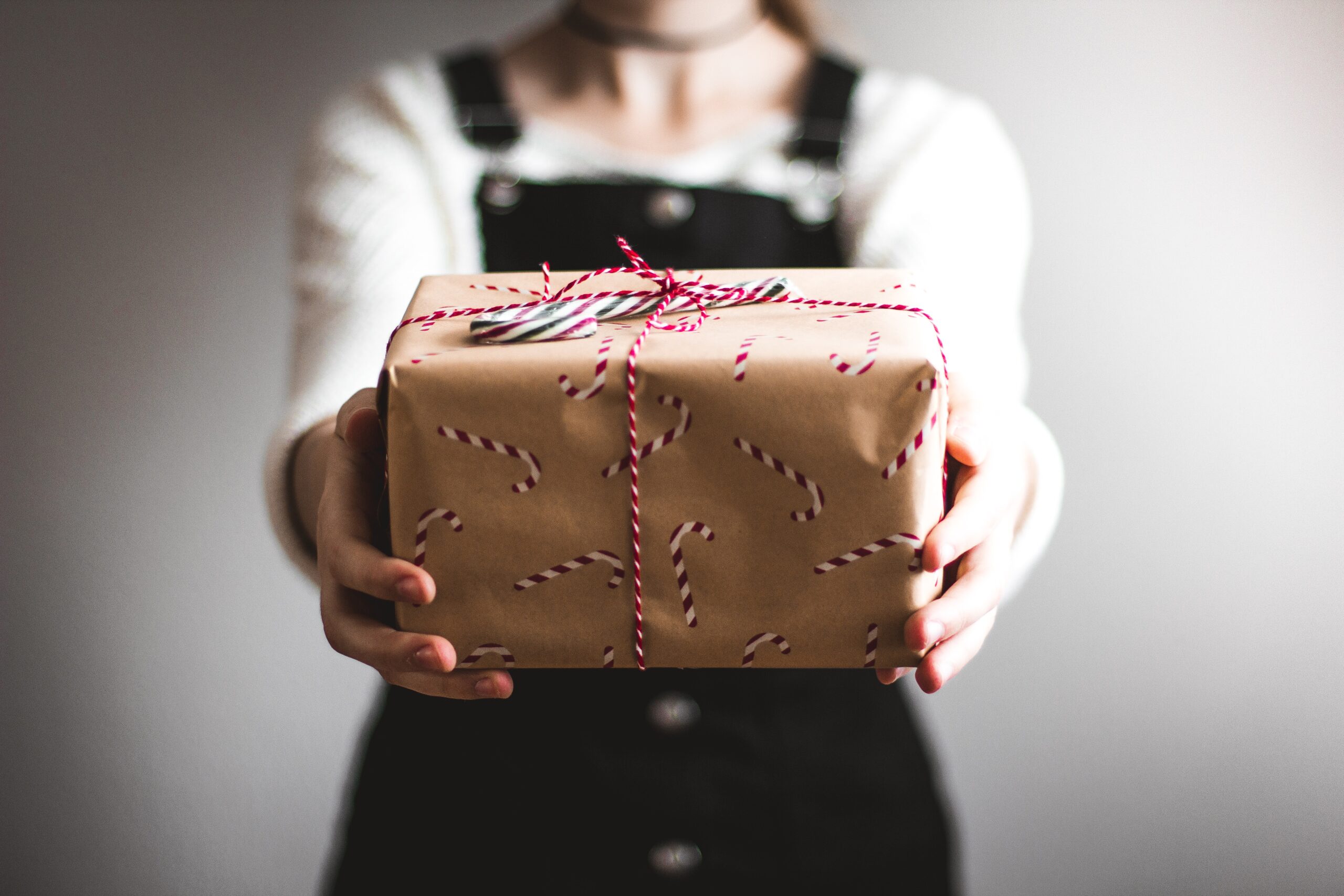 girl holding out gift wrapped in brown paper with red string