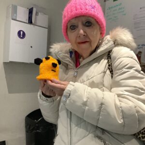 resident in pink woolly hat and white coat holding yellow knitting