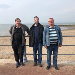 3 male residents on promenade in front of beach