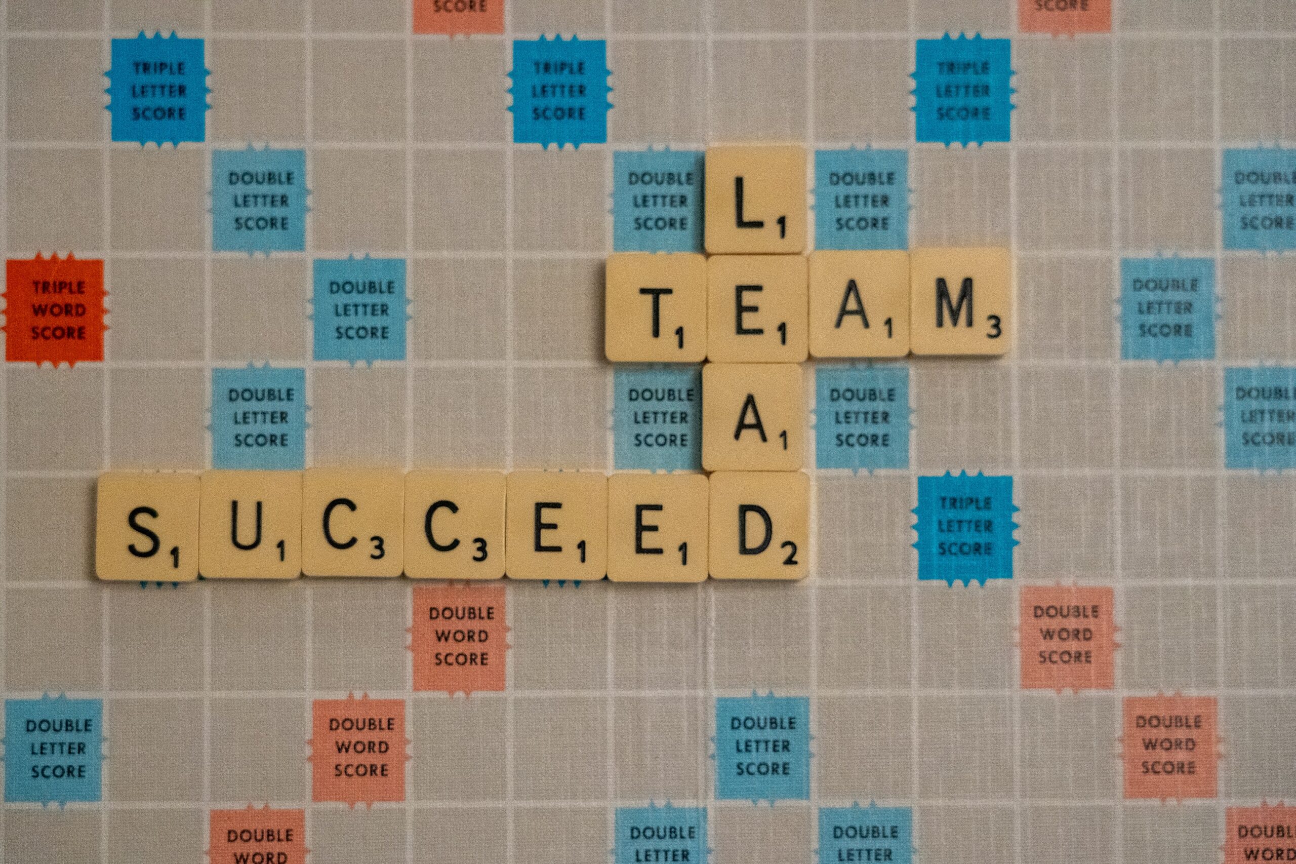 scrabble tiles on board spelling Team, Lead, Succeed
