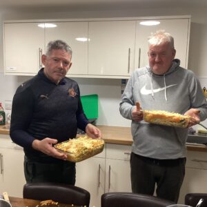 2 male residents holding dishes of homemade pasta