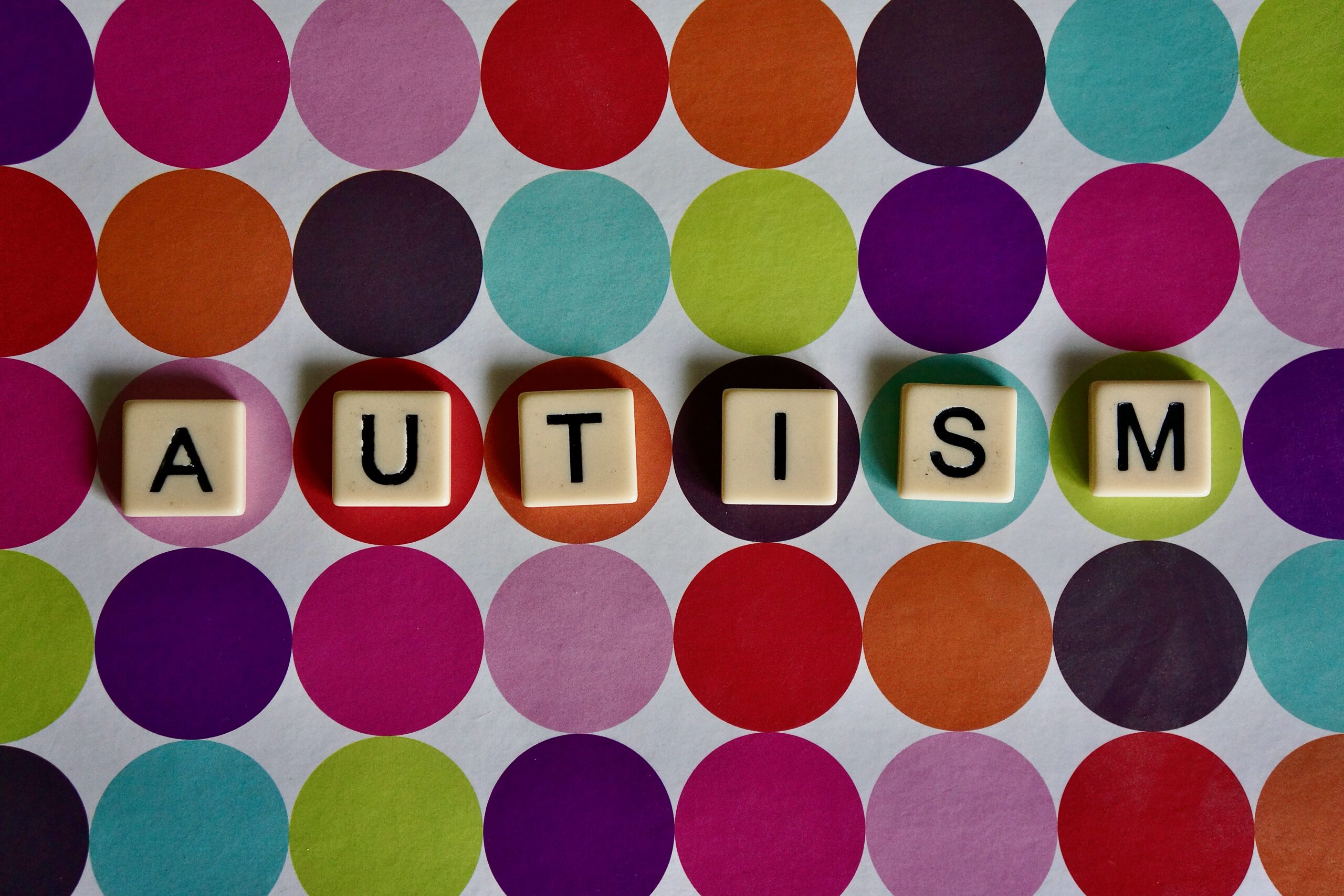 tiles spelling the word autism on colourful dots background