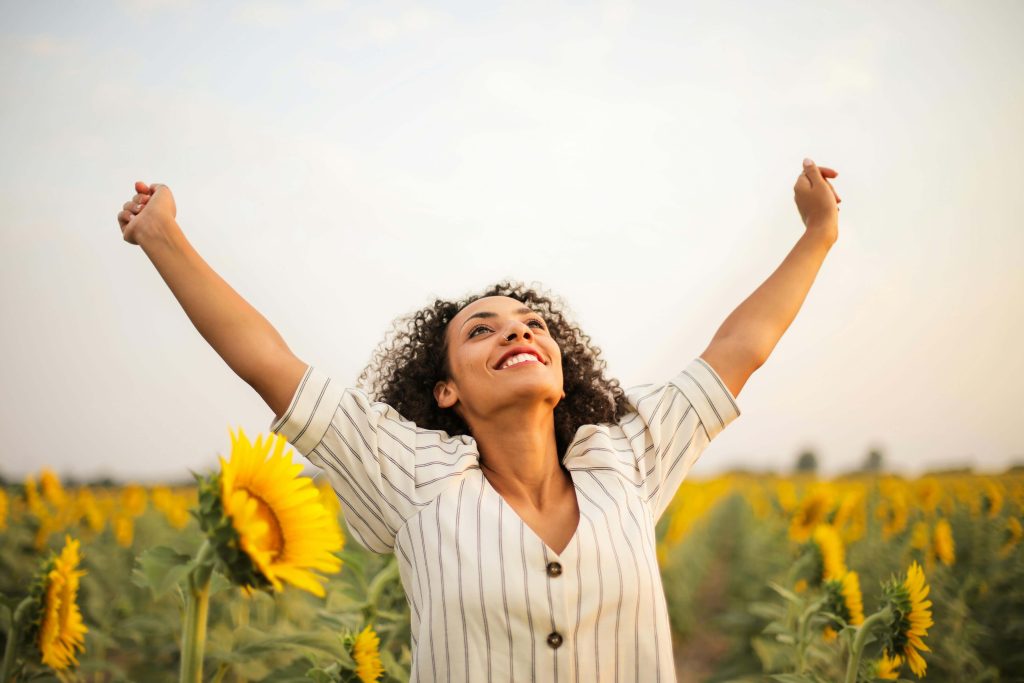 Woman in sunflower field celebrating with her arms in the air for a blog about acknowledging successes and achievements in supported living.