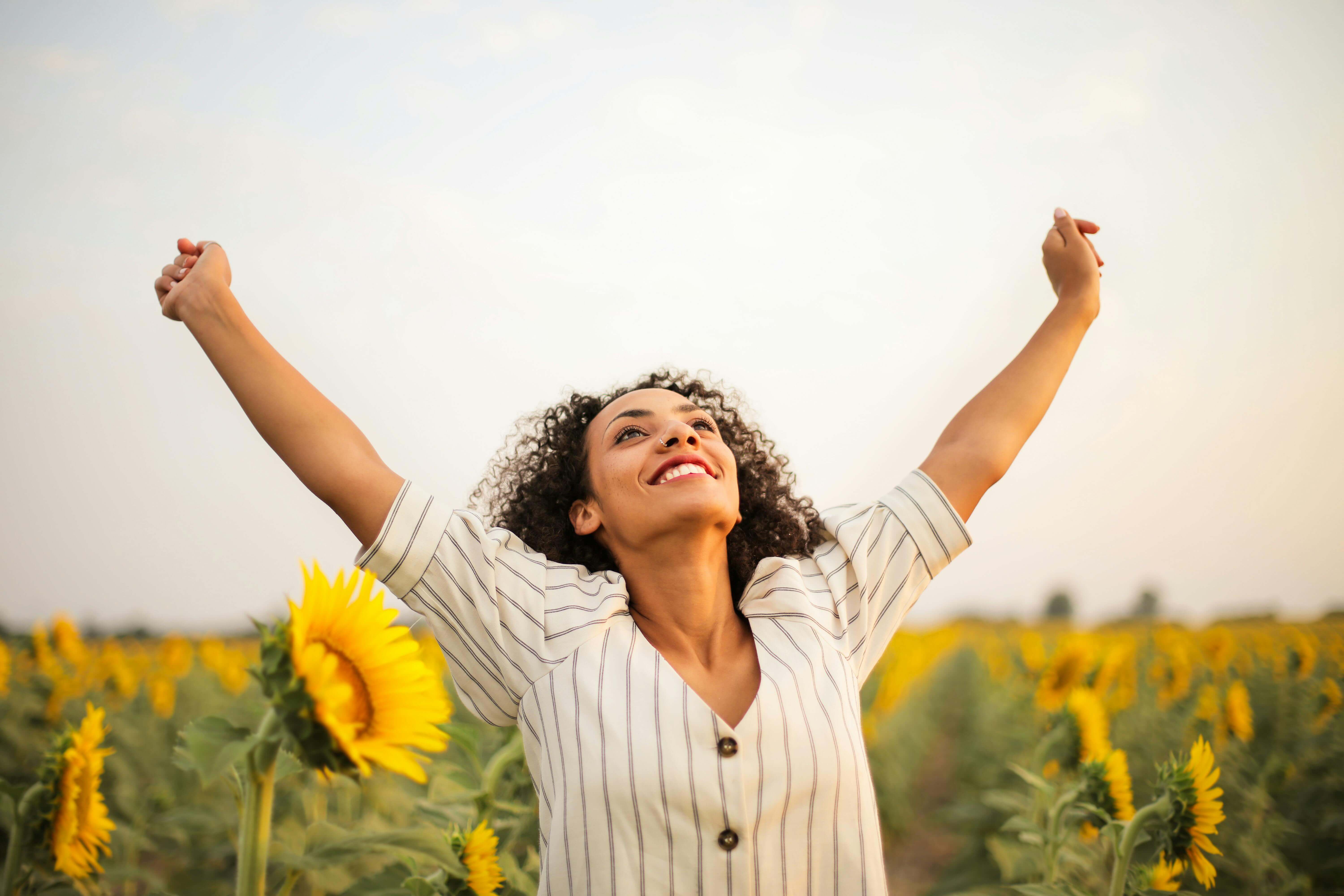 Woman in sunflower field celebrating with her arms in the air for a blog about acknowledging successes and achievements in supported living.