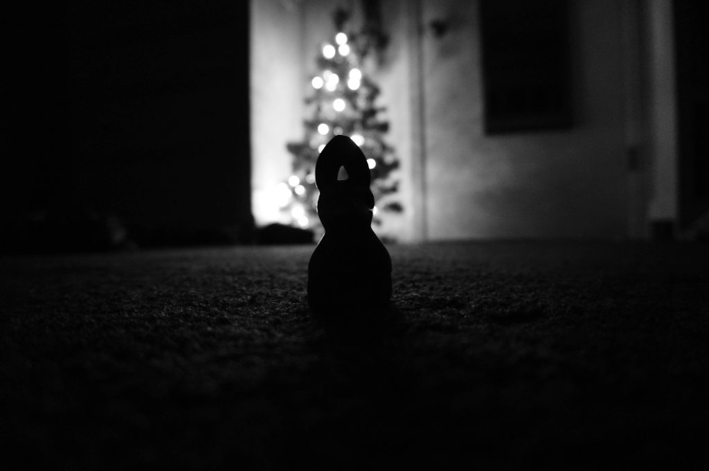 A toy looking at a Christmas tree in dramatic lighting in black and white to represent loneliness over the festive holidays.