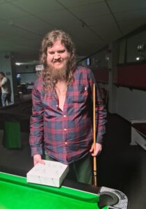 resident in check shirt standing behind pool table holding pool cue