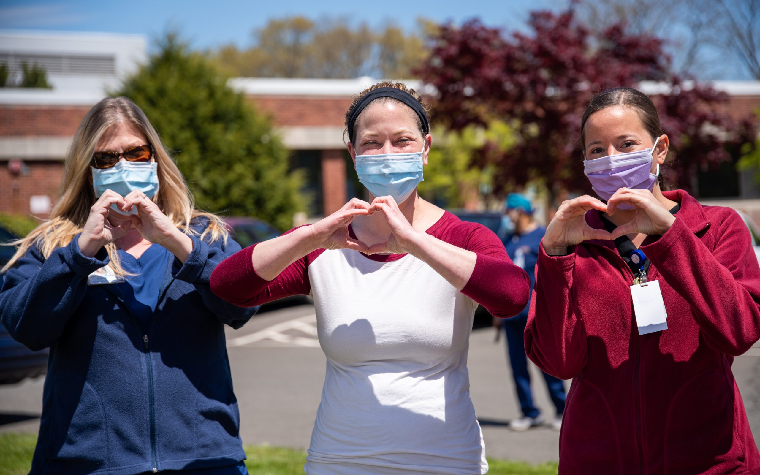 care workers on street wearing masks making heart shape with hands