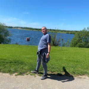 male in front of lake with blue sky and green grass