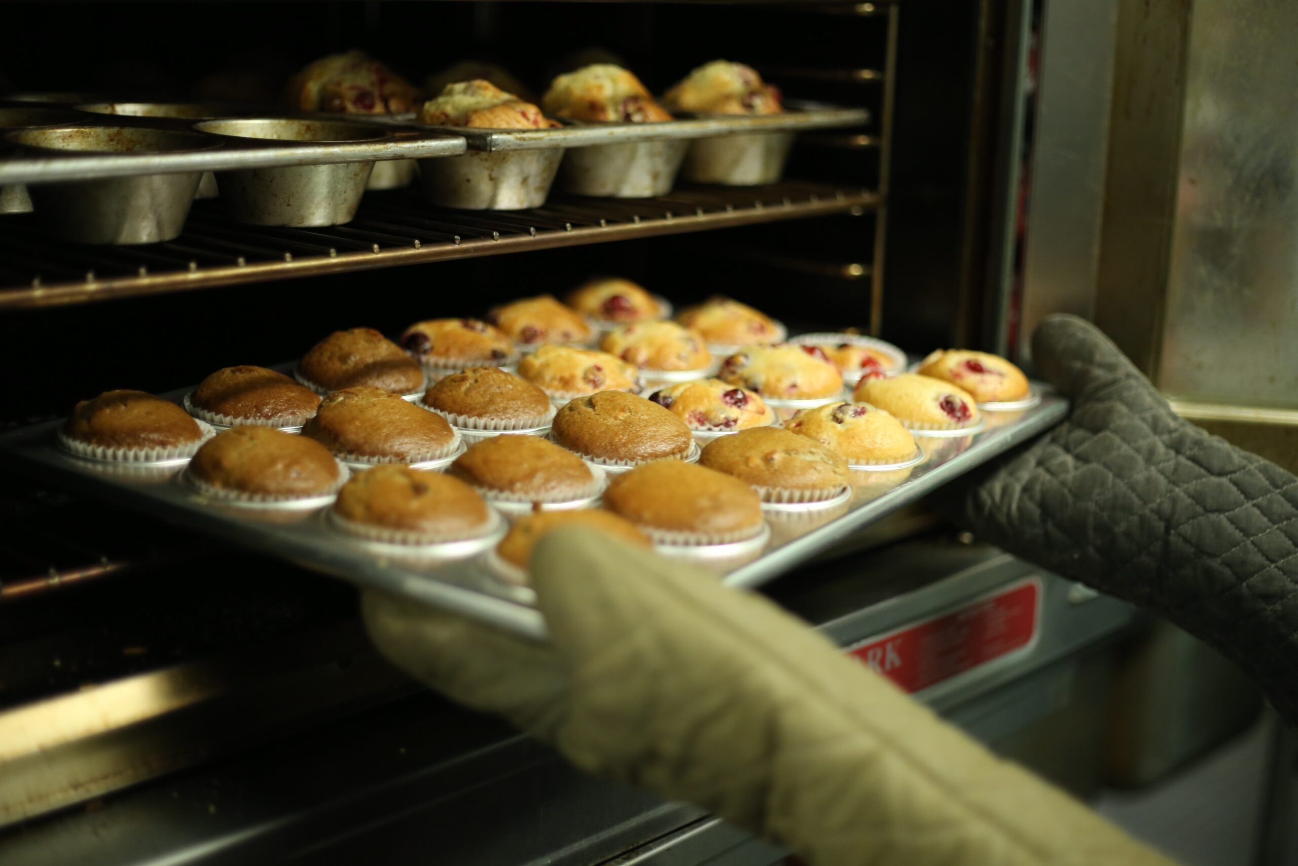 person wearing oven gloves taking tray of muffins out of oven
