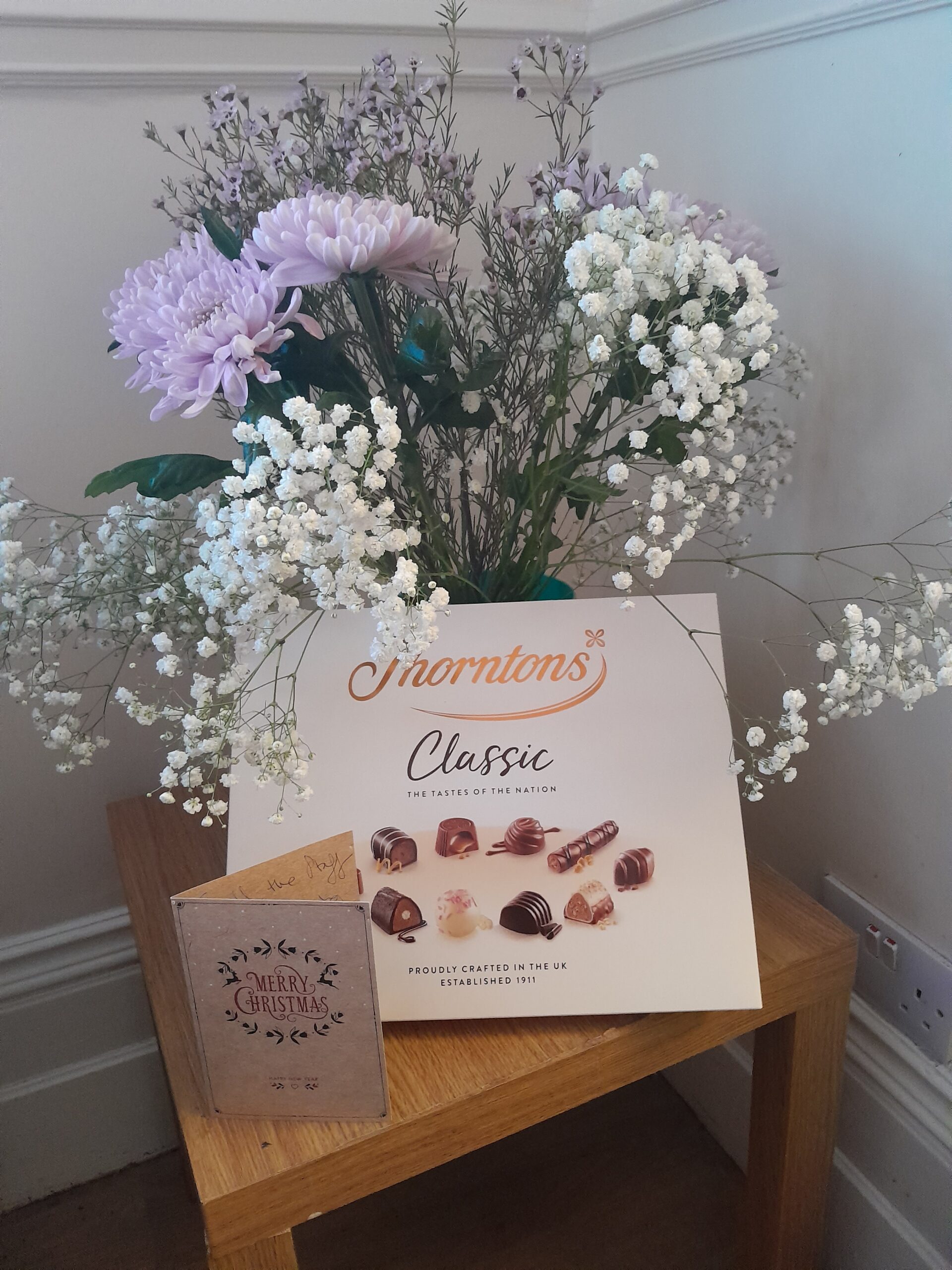 thank you card, box of chocolates and bunch of flowers on table