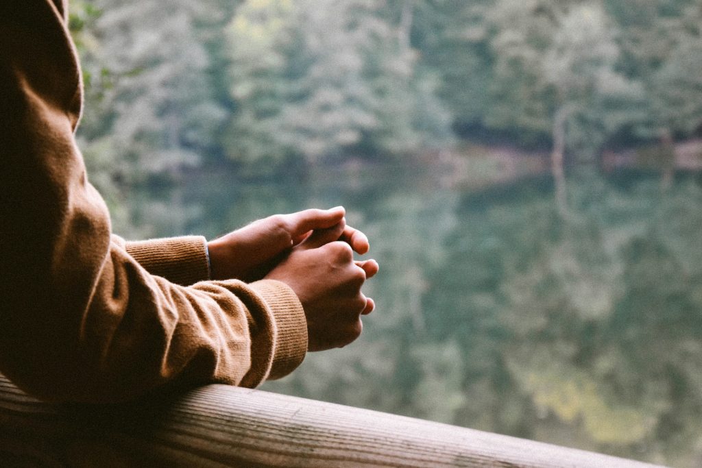 Hands close up of someone looking over a lake, representing how early life experiences affect mental health in adulthood.