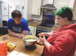 One resident making cookies while another resident watches