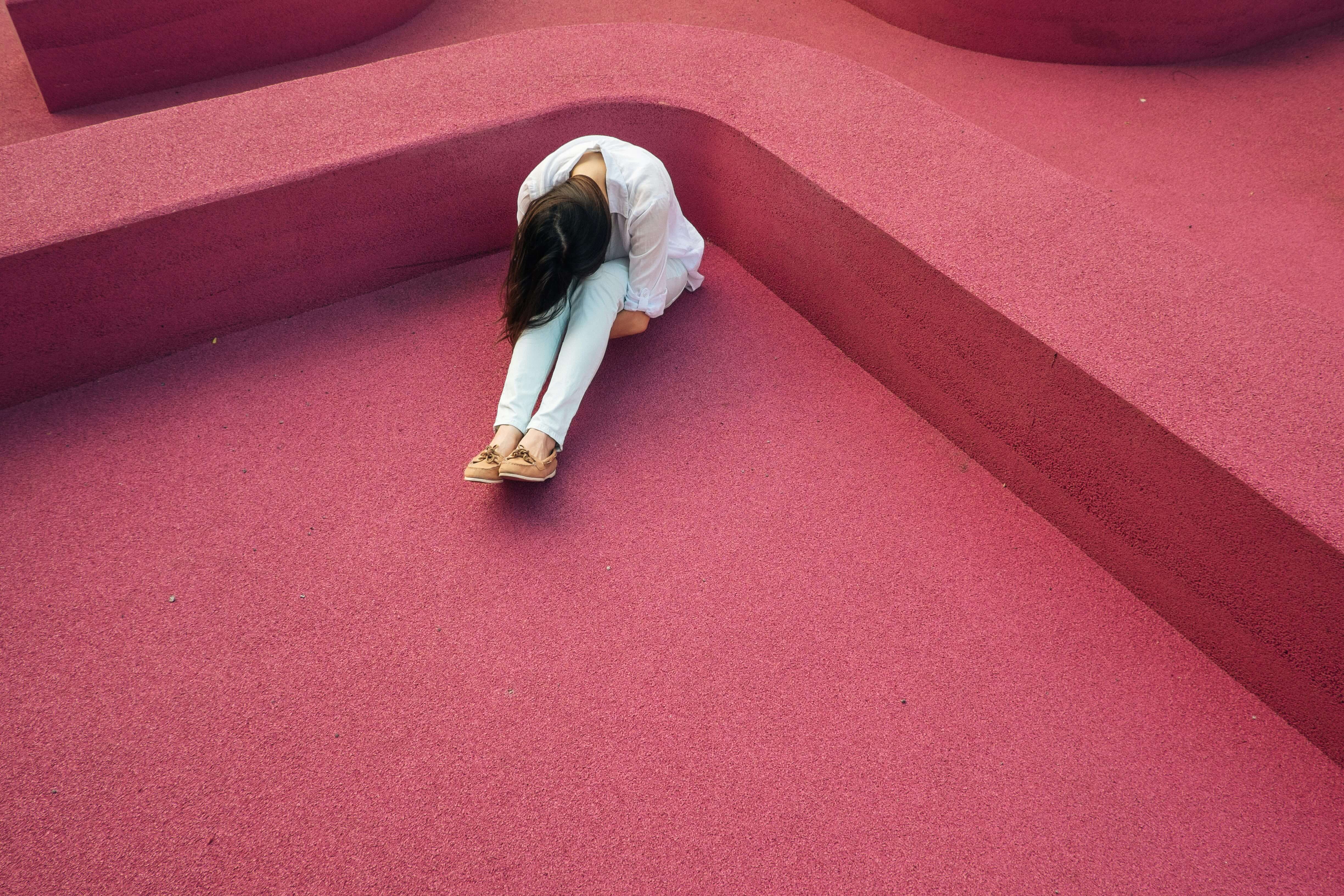 Girl sat in a corner on the floor with her head down to represent burnout in health and social care.