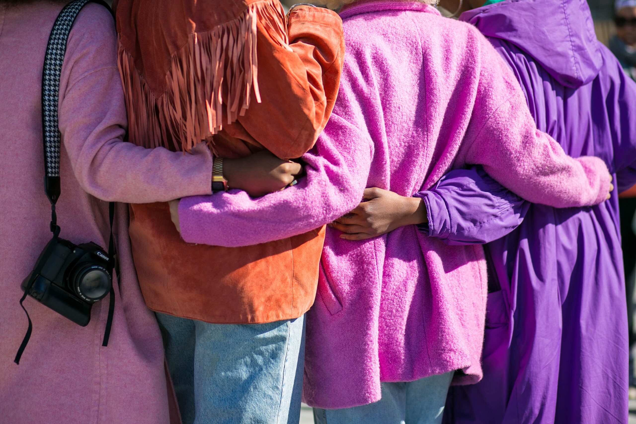a group of women in pink and orange coats hugging
