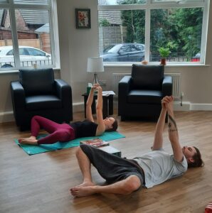male and female in yoga pose - laying flat on back with knees bent and arms clasped above