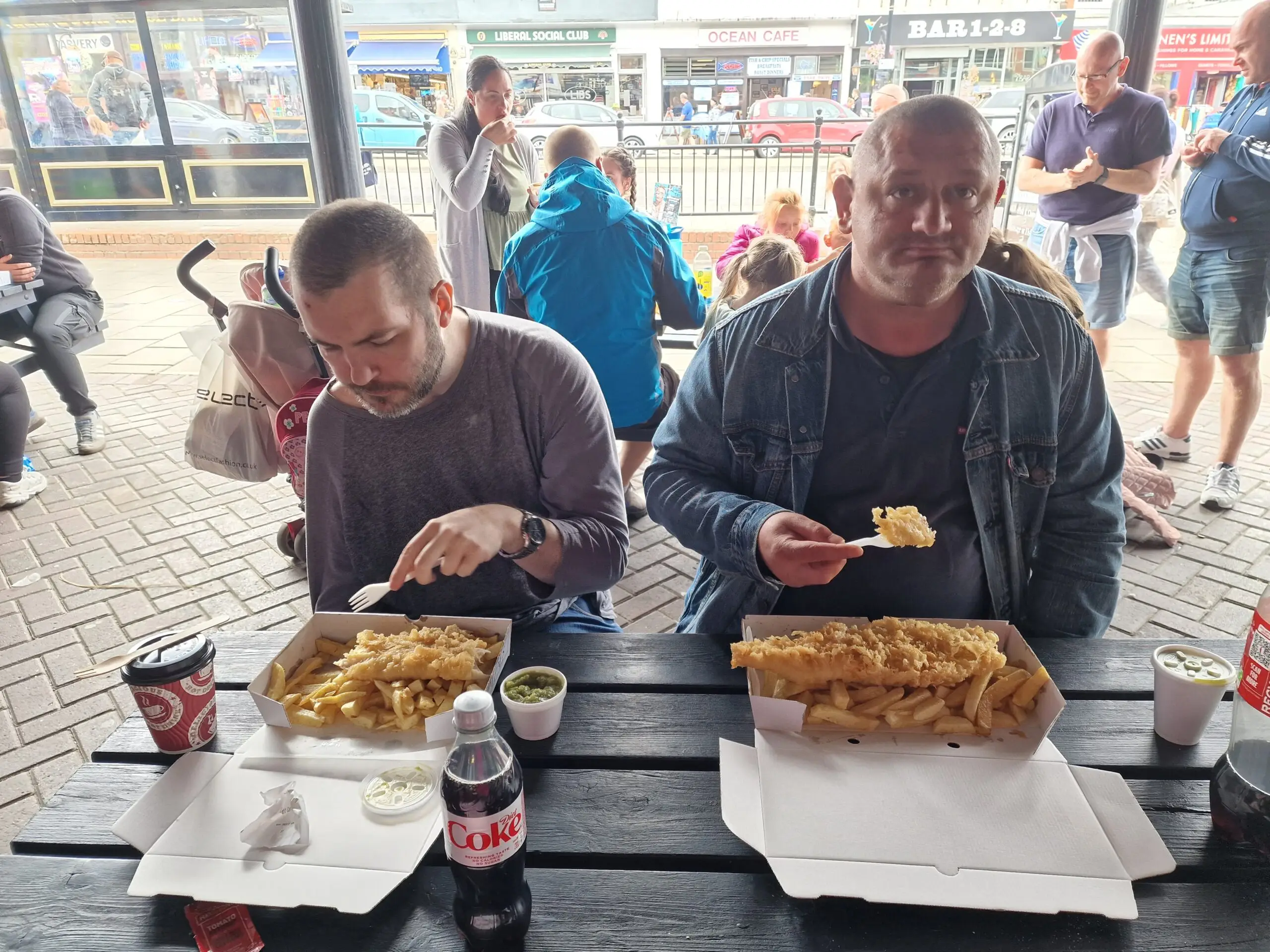 two male residents eating fish and chips on picnic bench